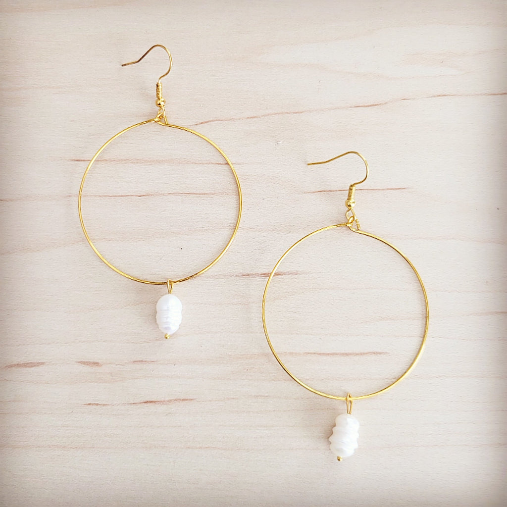 Gold-tone hoop earrings featuring a single freshwater pearl dangle on a wooden background