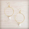 Gold-tone hoop earrings featuring a single freshwater pearl dangle on a wooden background
