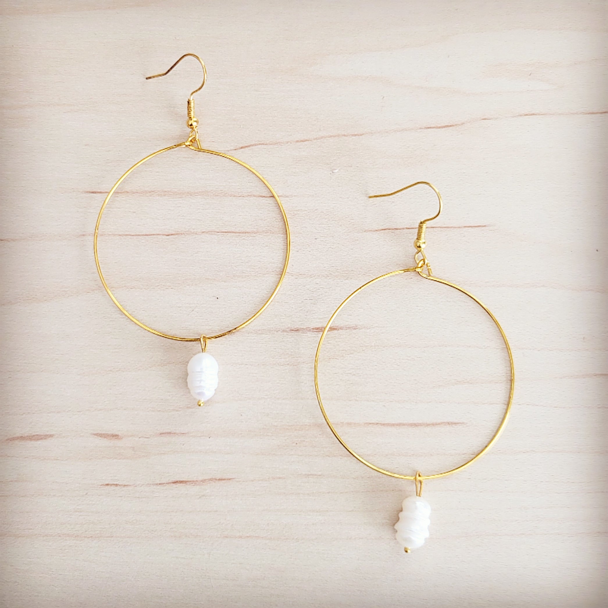 Gold-tone hoop earrings featuring a single freshwater pearl dangle on a wooden background