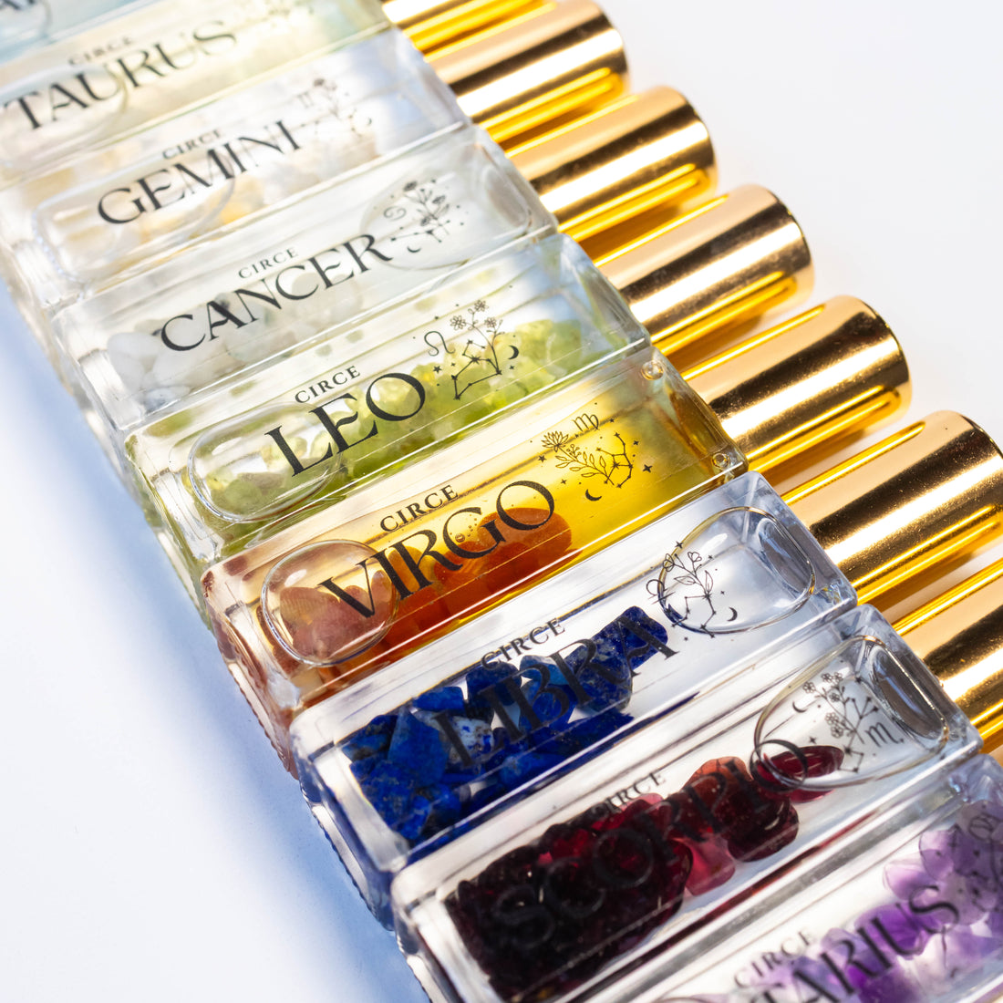 A collection of Circe Boutique Zodiac perfume rollerball bottles featuring various gemstones inside each clear glass vial with gold caps.