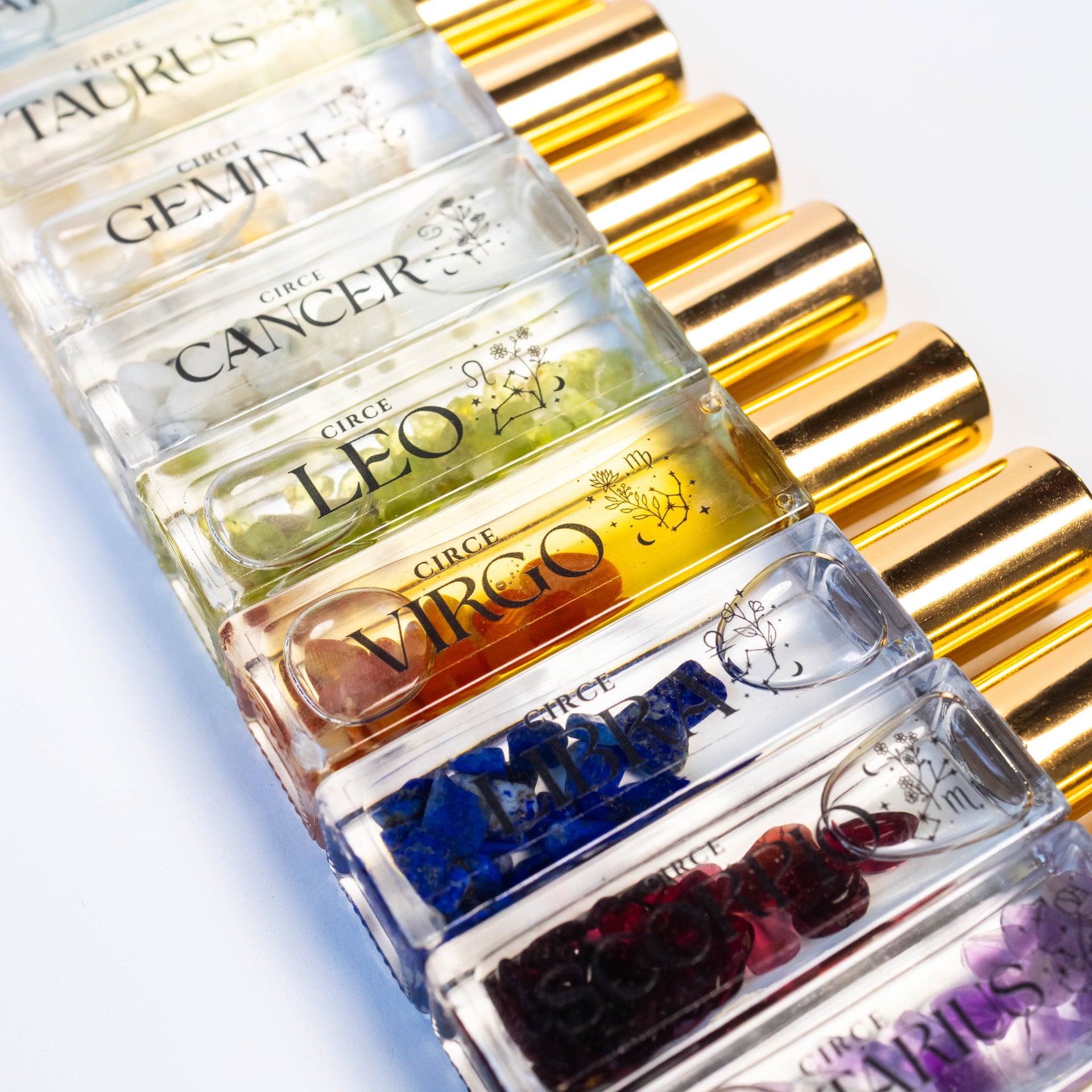 A collection of Circe Boutique Zodiac perfume rollerball bottles featuring various gemstones inside each clear glass vial with gold caps.