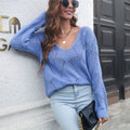 A woman wearing a blue hollow leaf pattern V-neck long sleeve knit sweater standing outside.