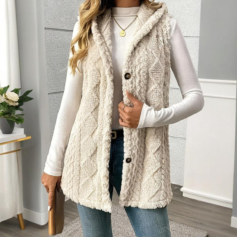 A woman wearing a textured beige sleeveless hooded vest with a button-front closure layered over a white long-sleeve top.