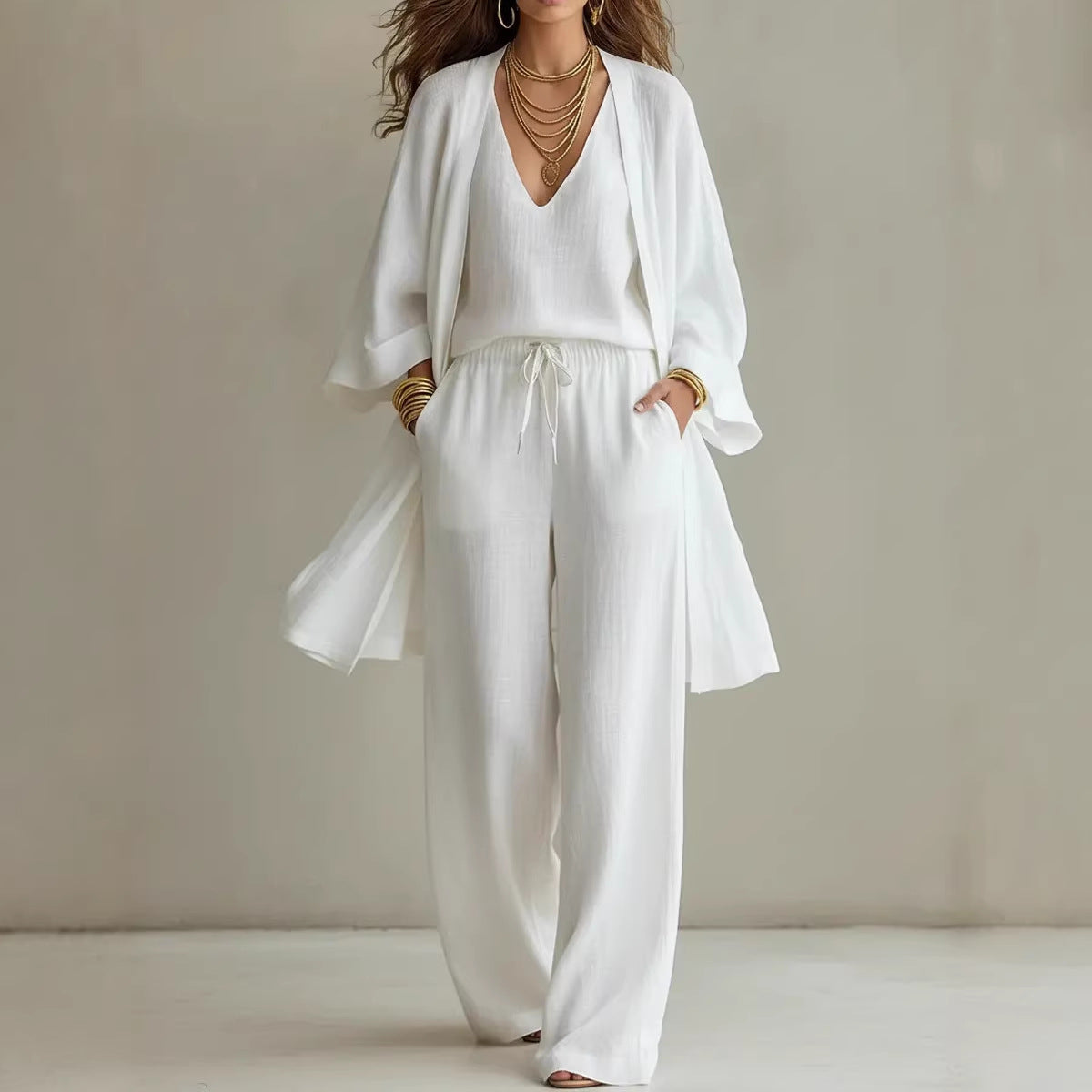A woman wearing a three-piece set consisting of a long V-neck cardigan, a matching vest, and loose, wide-leg drawstring pants.