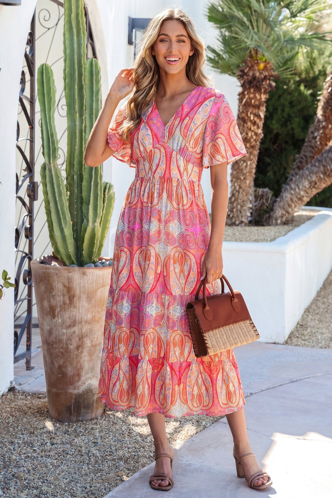 A woman wearing a vibrant, flowy boho midi dress with flutter sleeves in a sunset color palette against a vacation background.
