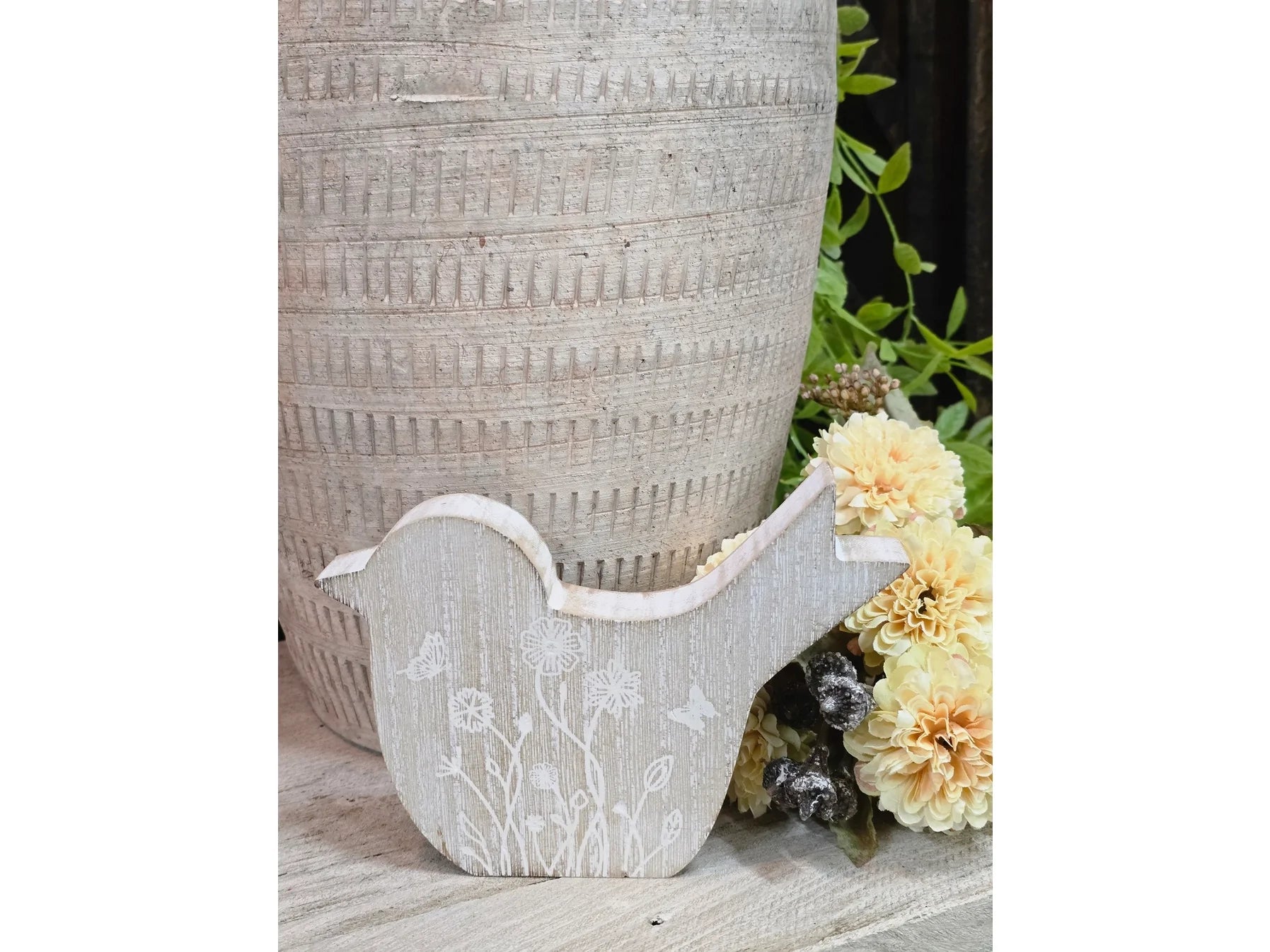 Small wooden bird figurine with a whitewashed rustic finish and white floral details sitting on a wooden surface.