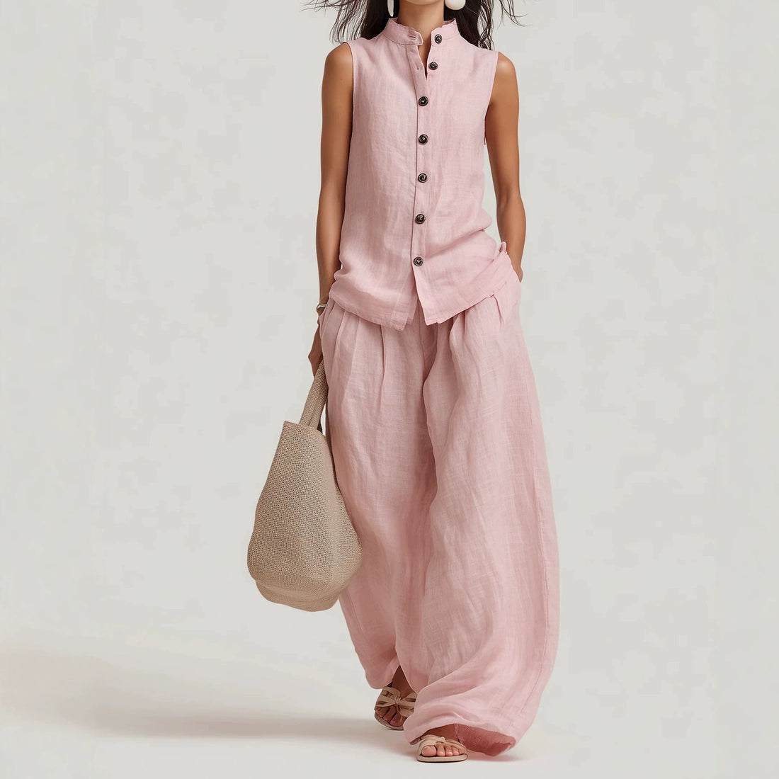 A woman wearing a matching light pink cotton-linen sleeveless button-down vest and wide-leg pants set with a woven bag.