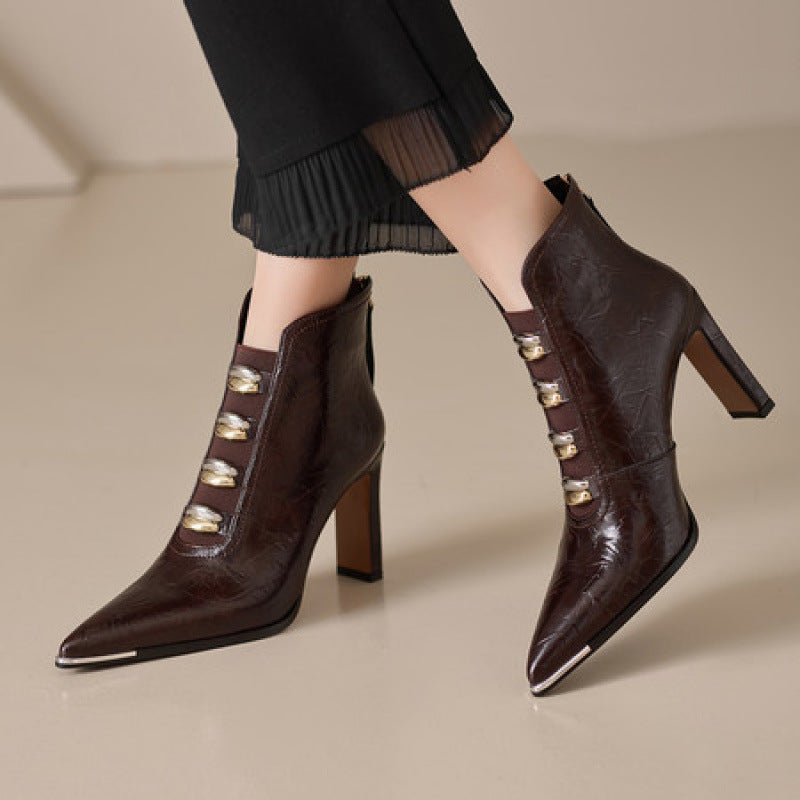 Close-up of women's black and brown pointed-toe ankle boots with chunky heels and gold-tone metal hardware accents.