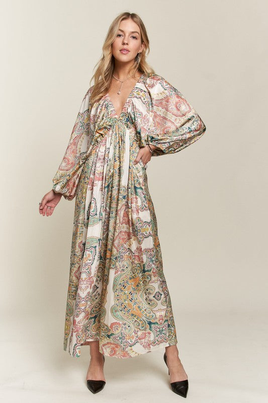 Woman wearing an abstract print satin V-neck dress with batwing sleeves in cream, orange, teal, and yellow.