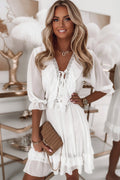 A woman wearing a white V-neck mini dress with ruffled details and intricate lace trim on the neckline.