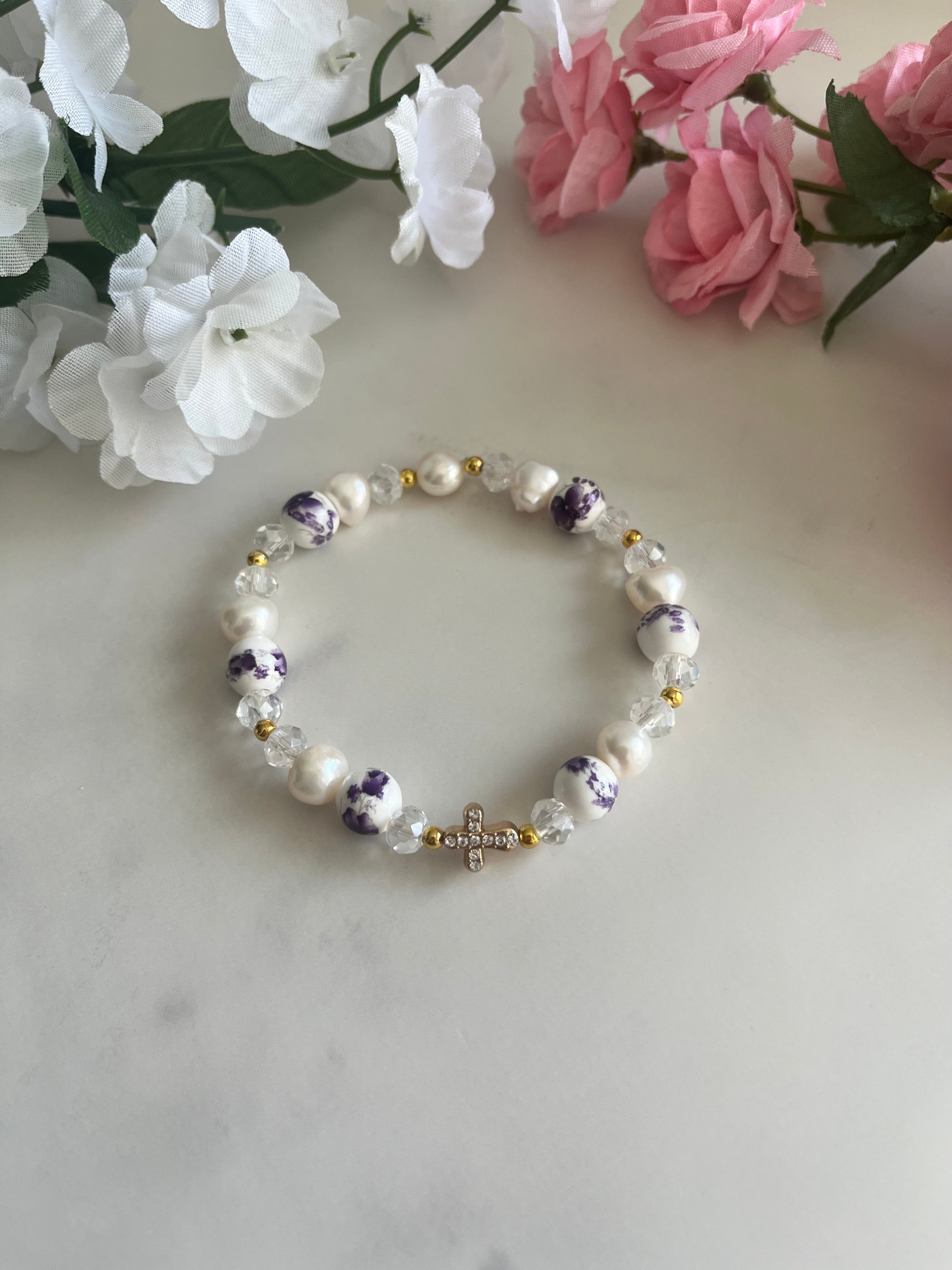 A romantic freshwater pearl bracelet featuring floral ceramic beads, a gold cross charm, and sparkling crystal accents.