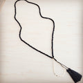 A black faceted bead lariat necklace with a gold-tone hammered teardrop charm and black fabric tassels.