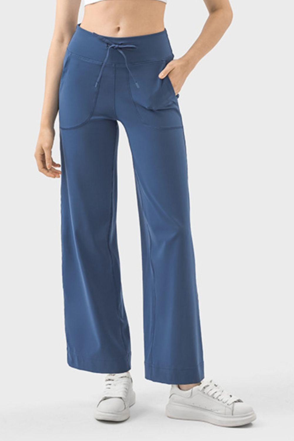 Model wearing blue drawstring active pants with side pockets paired with a white sports bra and white sneakers.