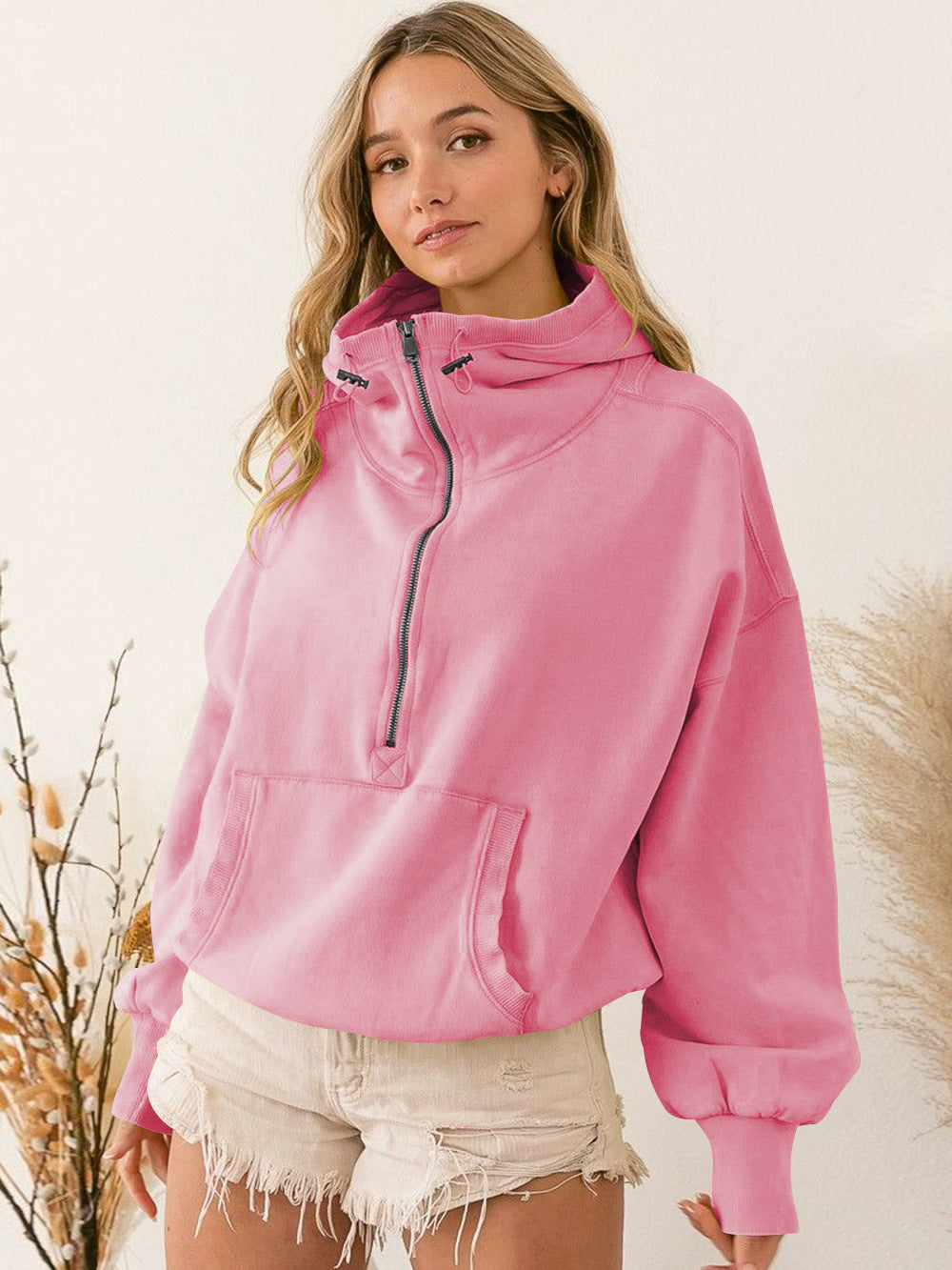 A woman wearing a pink quarter zip stand collar hoodie with a front kangaroo pocket.