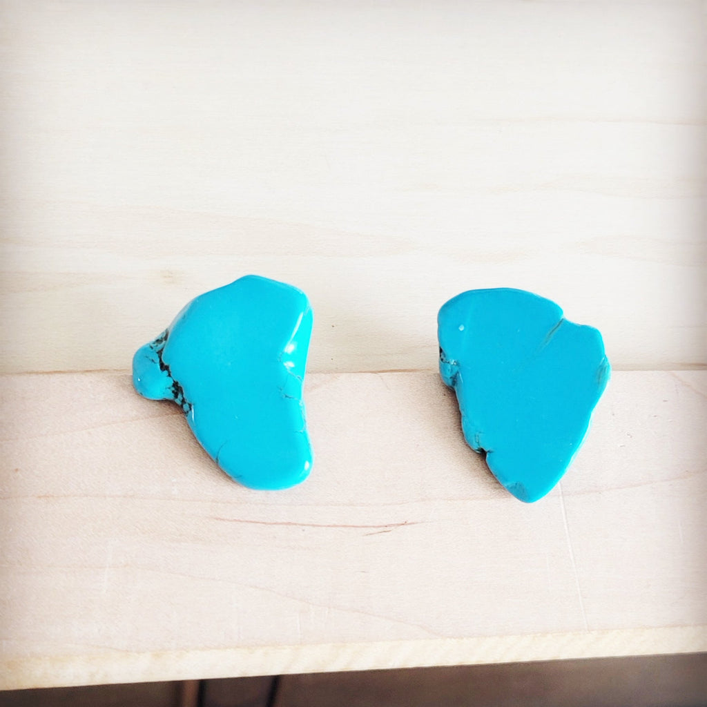 A pair of bright blue natural Turquoise slab stud earrings shown from the front and back on a light wood background.