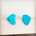 A pair of bright blue natural Turquoise slab stud earrings shown from the front and back on a light wood background.