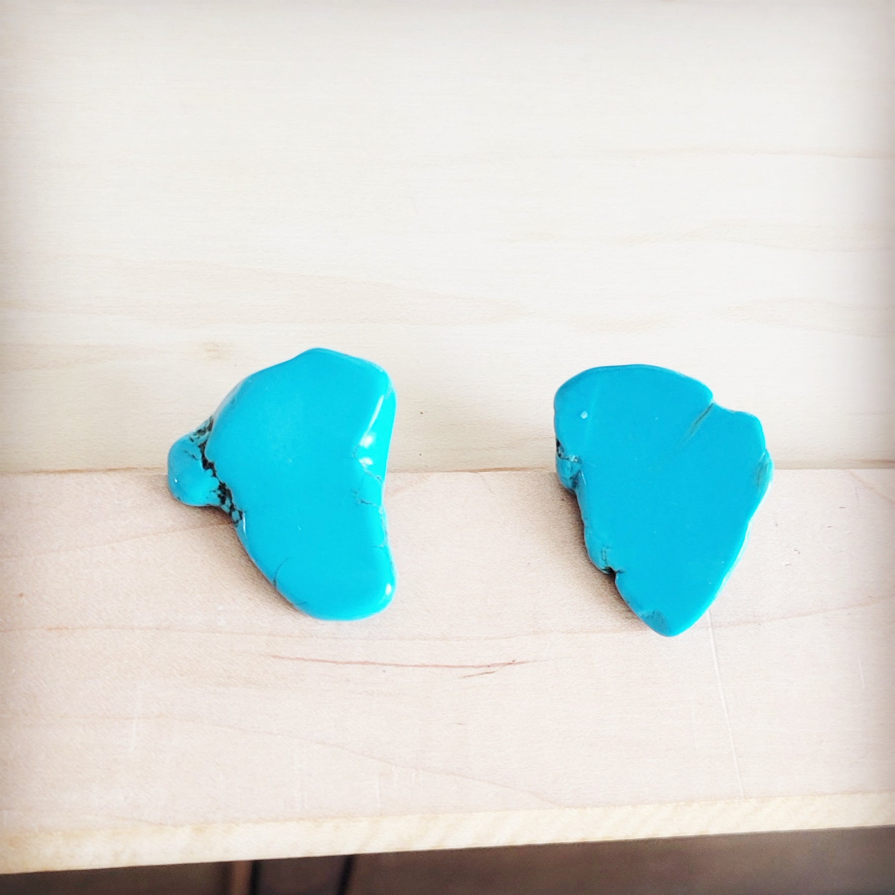 A pair of bright blue natural Turquoise slab stud earrings shown from the front and back on a light wood background.