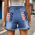 Close-up back view of blue denim shorts with US flag design on back pockets and frayed hem details.