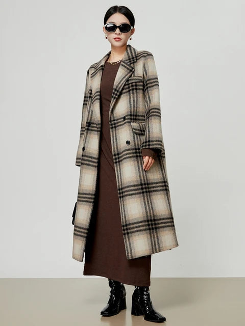 A woman wearing a long, double-breasted beige and black plaid wool blend coat with a notched collar over a brown dress, styled for a vintage Harajuku look.