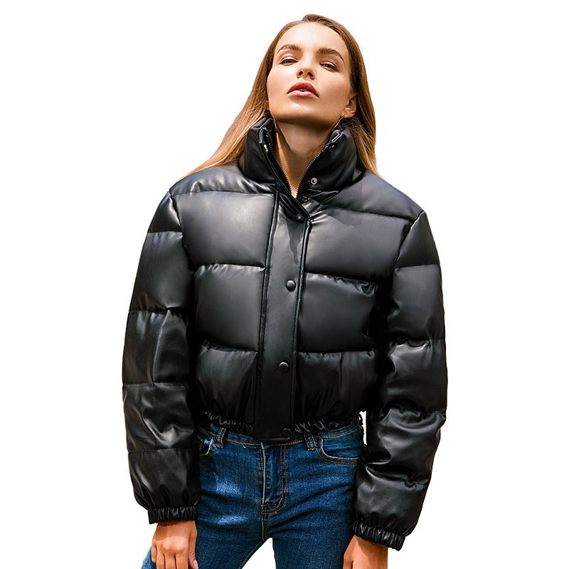 Women's Harajuku style cropped black and taupe puffer jacket with a standing collar, visible zipper and snap buttons, and a faux leather finish worn by a model in a street setting.