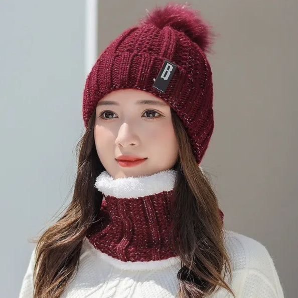A woman wearing a burgundy knitted winter beanie with a pom-pom and matching fleece-lined neck scarf.