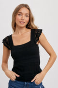A woman wearing a black square neck tank top with unique crossed strap detail.