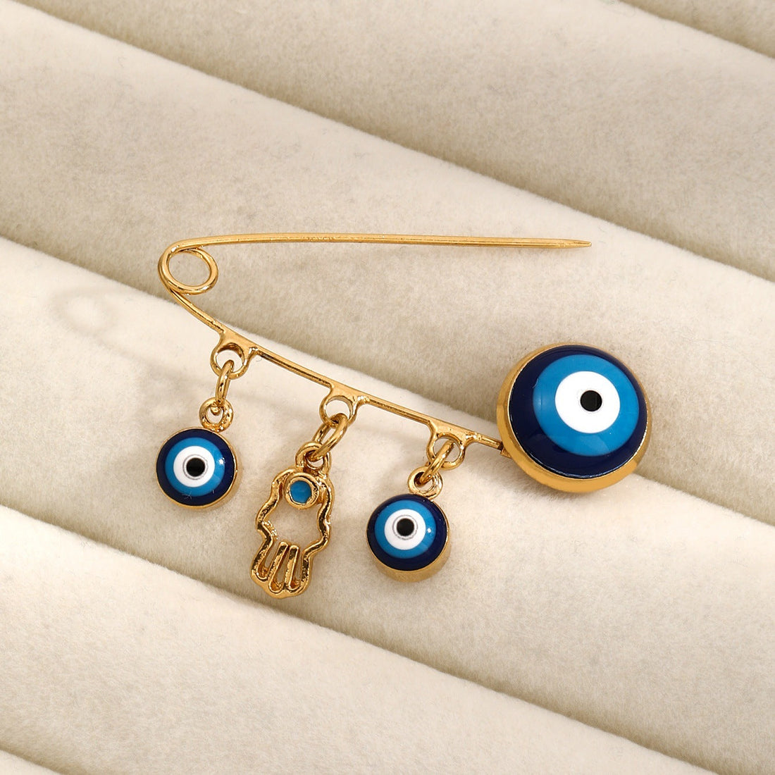 Gold-tone Evil Eye and Hamsa hand brooch pin with blue accents on a dark background