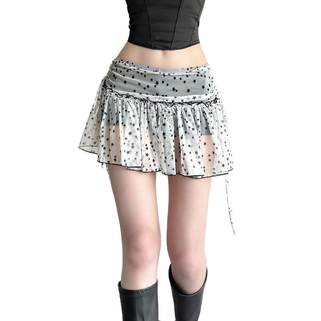 Model wearing a white star print pleated mini skirt with a sheer overlay and side drawstring, paired with a black crop top and black boots, showcasing a trendy Harajuku style.