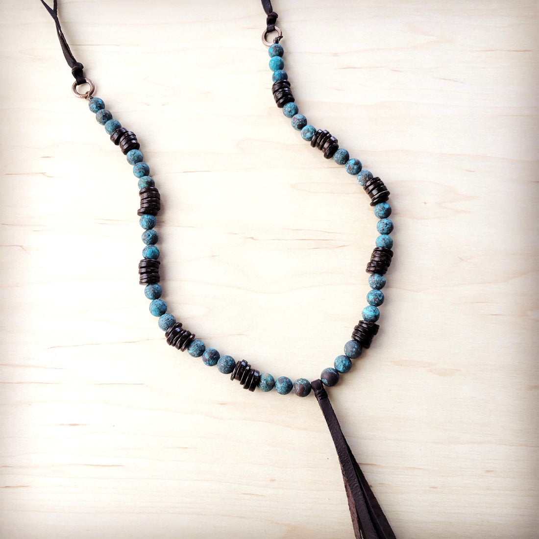Natural American turquoise beads with dark wood spacers and a leather tassel on a wooden background