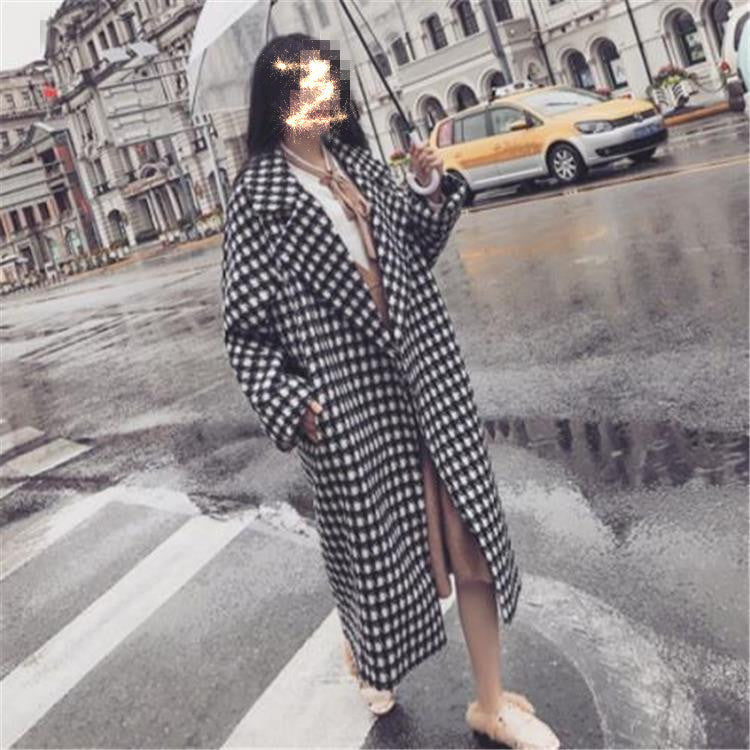 Woman wearing a Harajuku style black and white checkered woolen long coat walking on a city street with an umbrella.