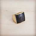 A gold-tone ring with a large square face completely set with black micro-pave crystals on a wooden background