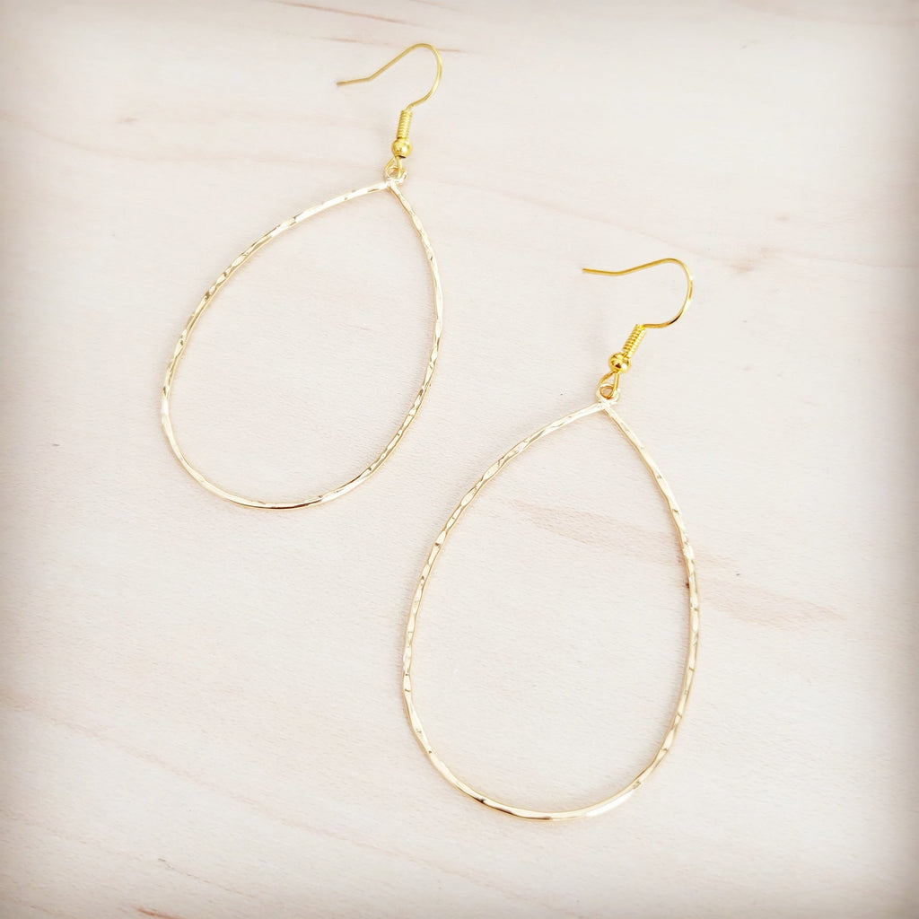 Hammered gold-tone oval teardrop hoop earrings on a light wooden background