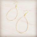 Hammered gold-tone oval teardrop hoop earrings on a light wooden background