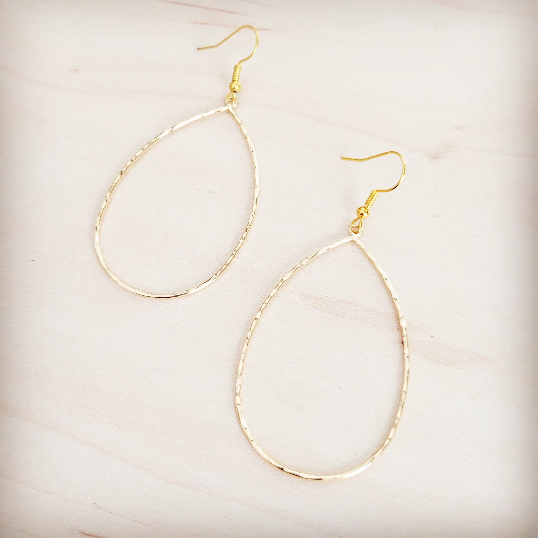 Hammered gold-tone oval teardrop hoop earrings on a light wooden background