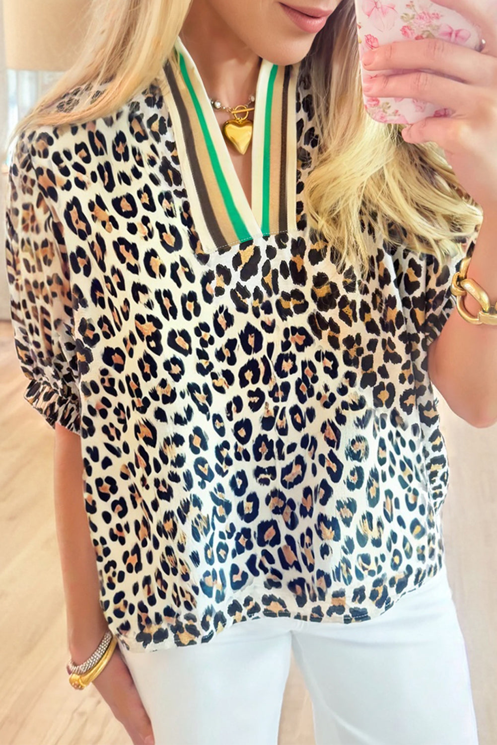 Woman wearing a loose-fitting leopard print blouse with a green and brown striped V-neck collar.