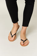 Close up of women's feet wearing simple black patent thong sandals with a tan sole.