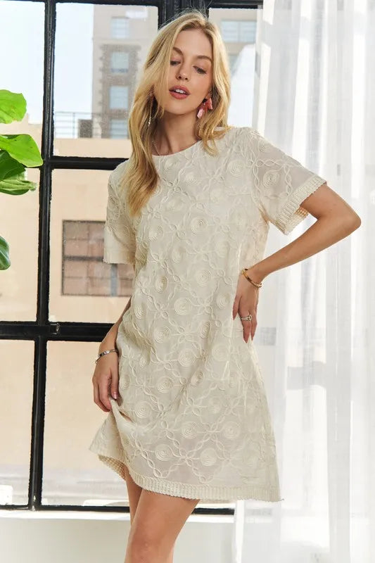 A cream-colored shift dress with sophisticated applique detailing and a classic round neckline.