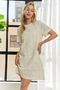 A cream-colored shift dress with sophisticated applique detailing and a classic round neckline.