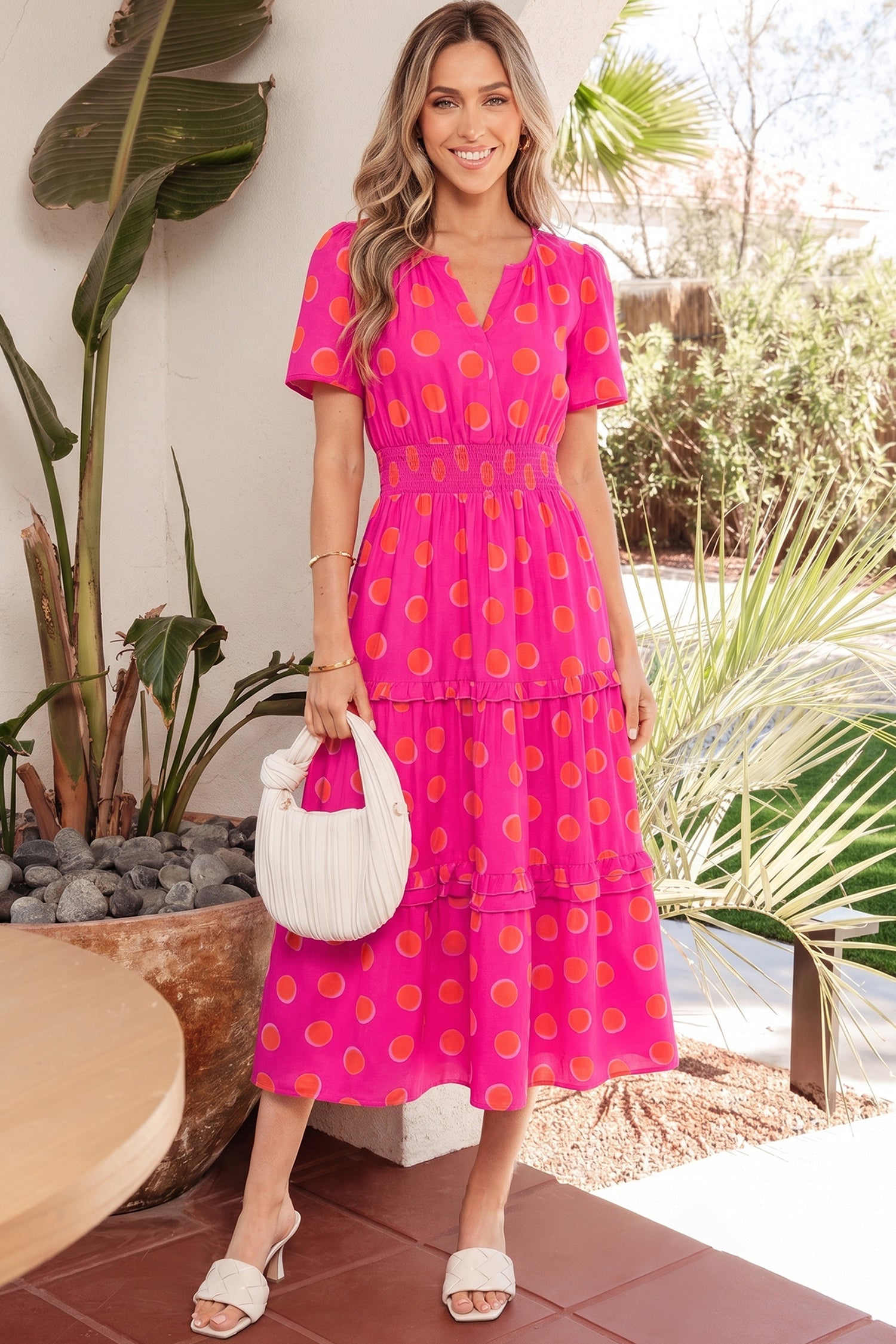 Woman wearing a vibrant neon pink midi dress with bright orange polka dots and a shirred waist.