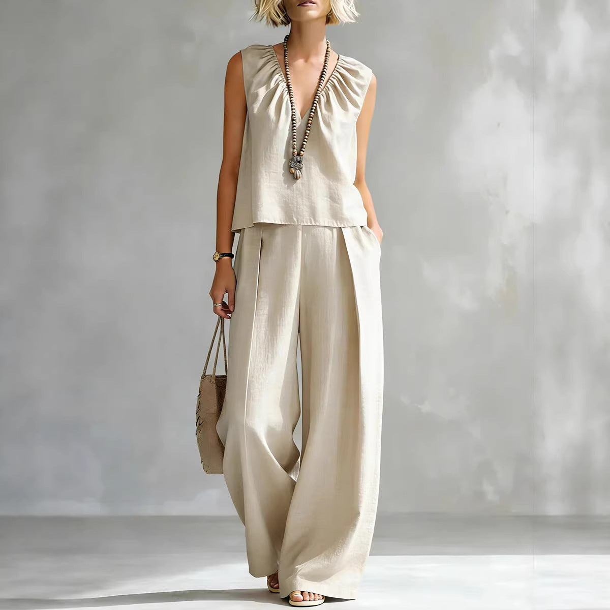 Model wearing a sleeveless cotton-linen top and matching wide-leg trousers in a neutral beige and soft blue colorway.