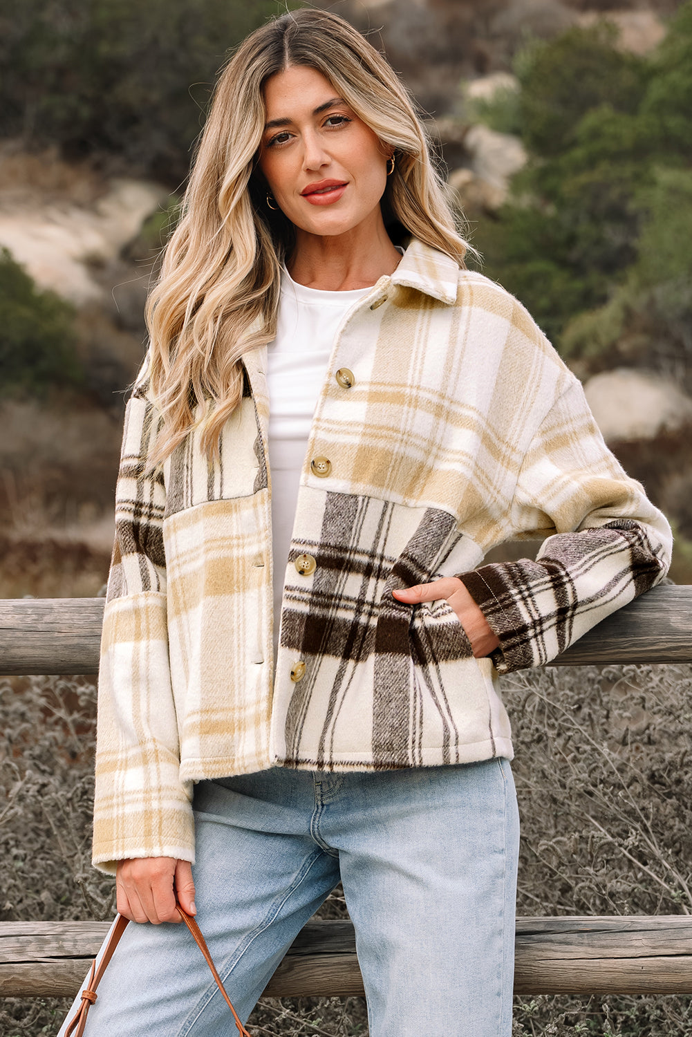 A woman wearing a cream, tan, and brown plaid patchwork shacket with button closure and side pockets.