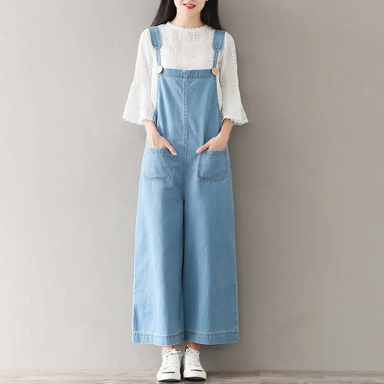 Model wearing a wide-leg denim overall jumpsuit with a light blue wash over a white top.