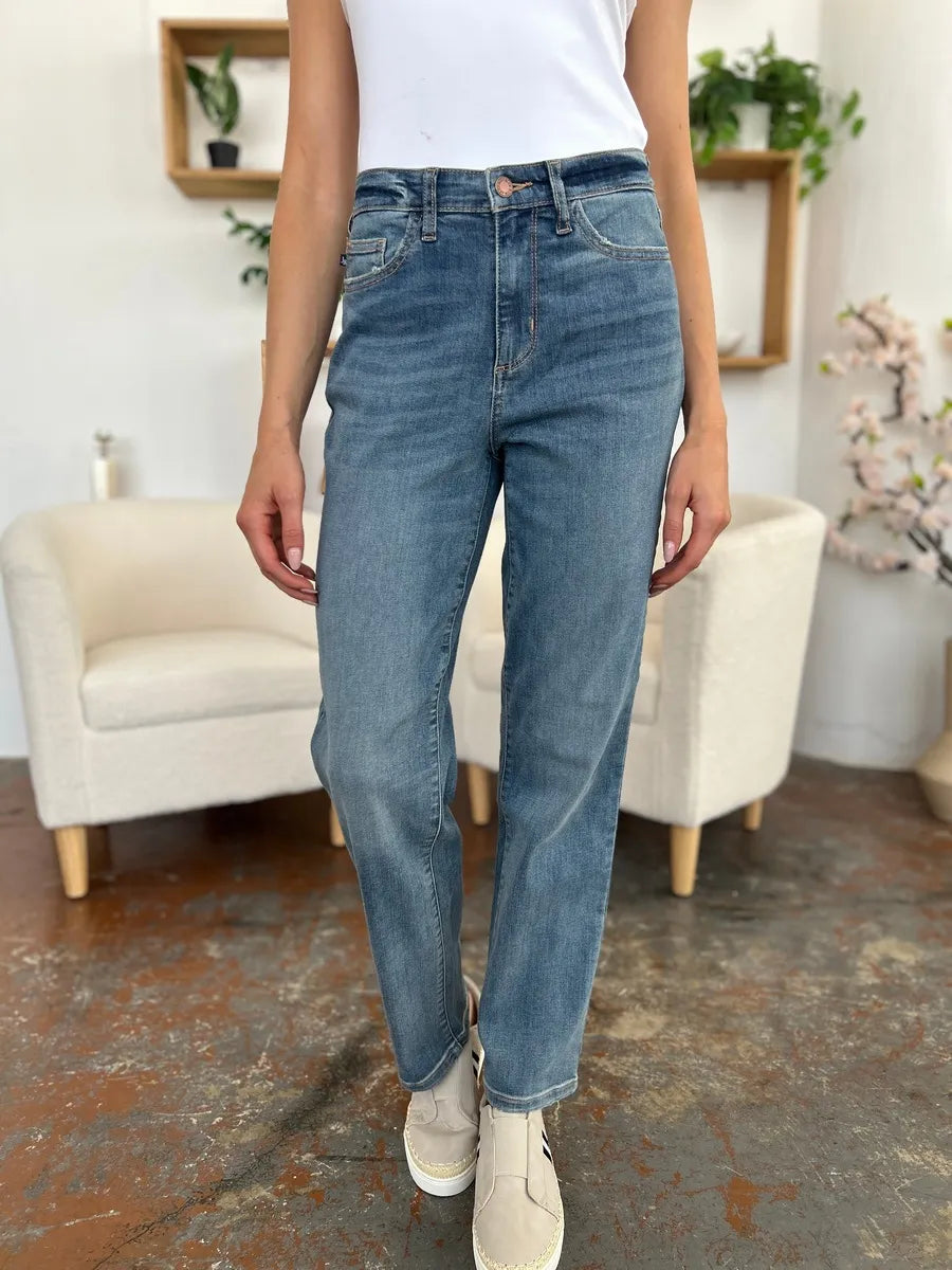 Person wearing blue jeans in a room with a white couch and decorative plants.