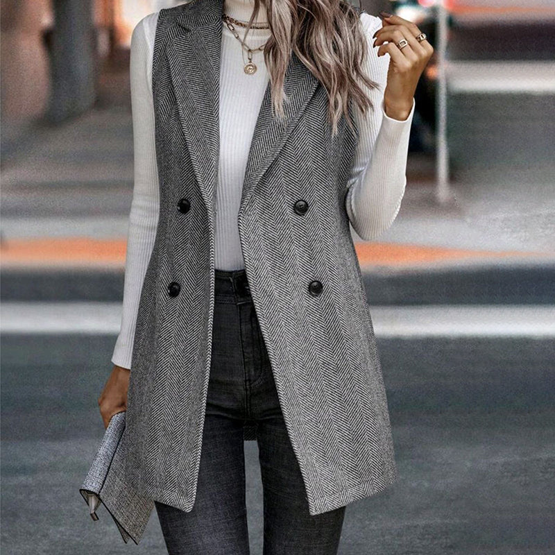 Model wearing a grey herringbone patterned sleeveless blazer vest over a white long-sleeve top.