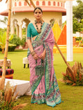 Woman wearing a salmon-pink silk patola saree with a contrasting deep teal V-neck blouse in a traditional setting.