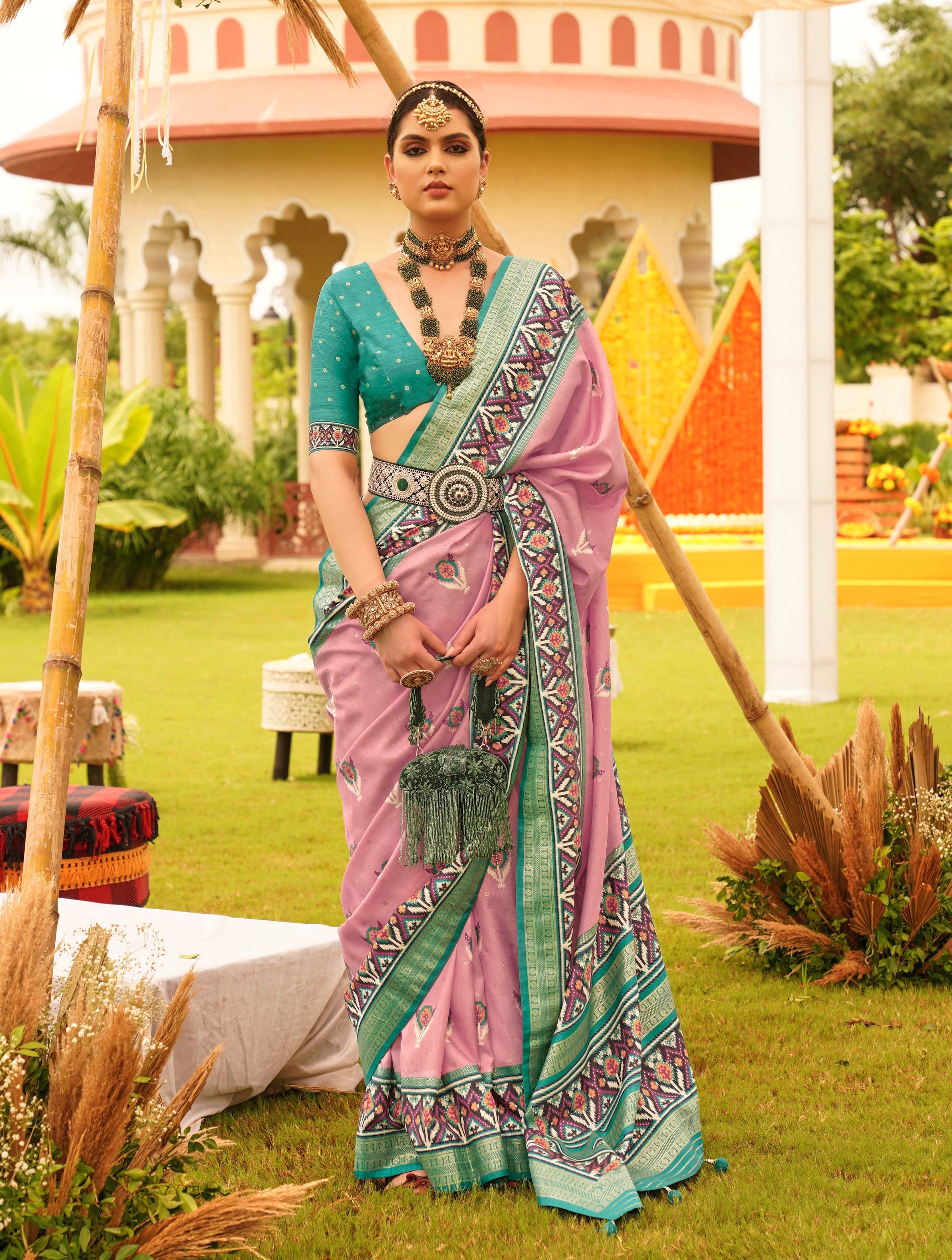 Woman wearing a salmon-pink silk patola saree with a contrasting deep teal V-neck blouse in a traditional setting.