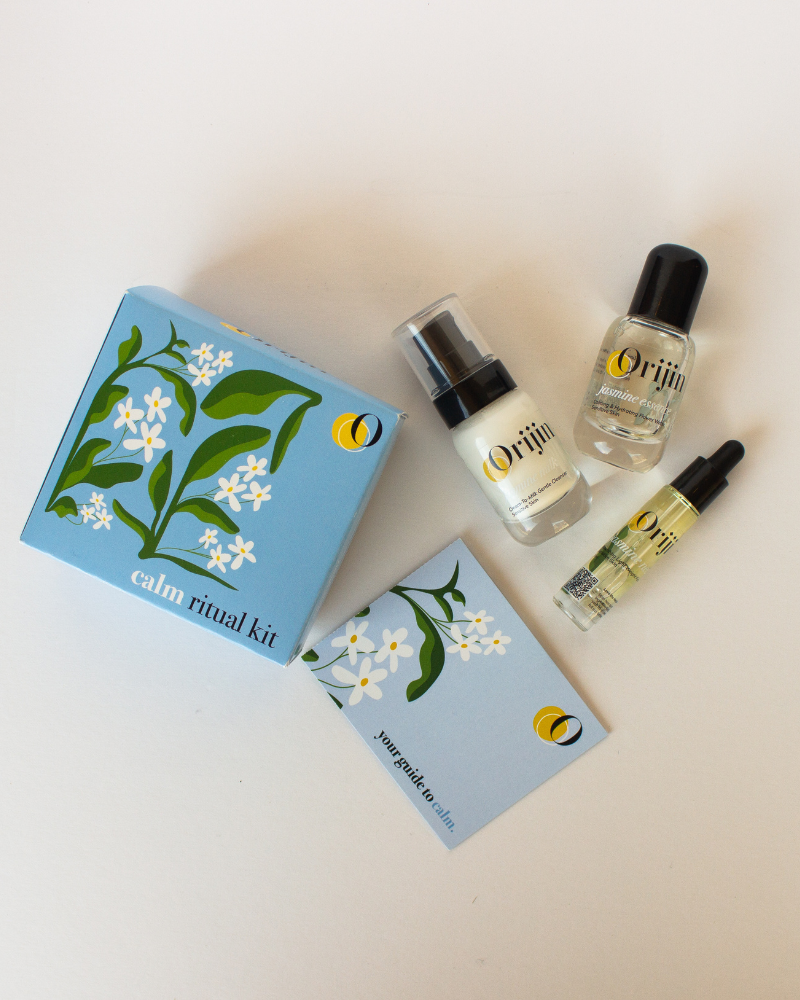 Orijin Calm Ritual Kit featuring three travel-sized jasmine skincare bottles and a guide, arranged next to a blue floral gift box.
