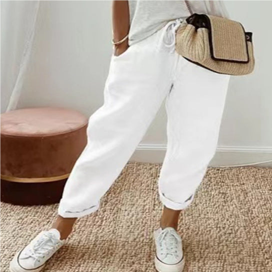A woman wearing relaxed-fit white cotton linen casual pants with a drawstring waist and rolled hems.