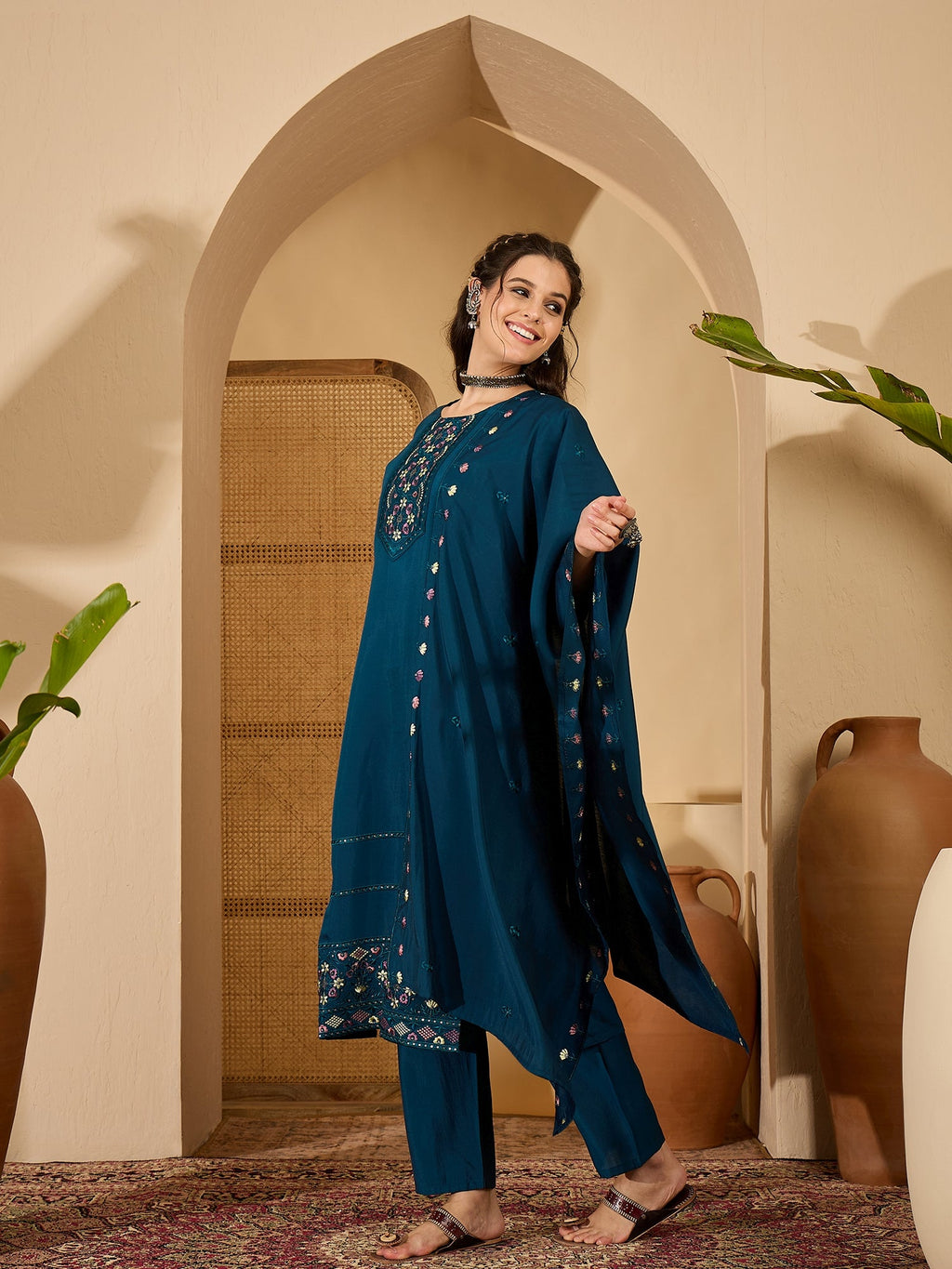 A woman wearing an elegant teal silk readymade kurta set with intricate embroidery around the round neckline.