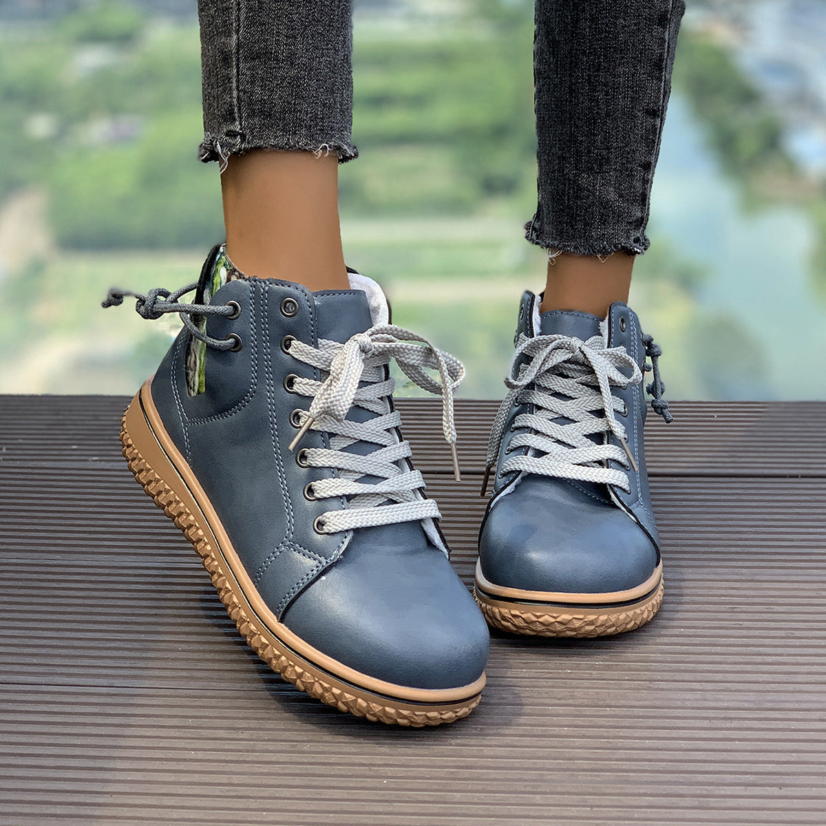 A pair of blue flat-heel lace-up Martin boots with a side zipper and textured sole, worn by a model.